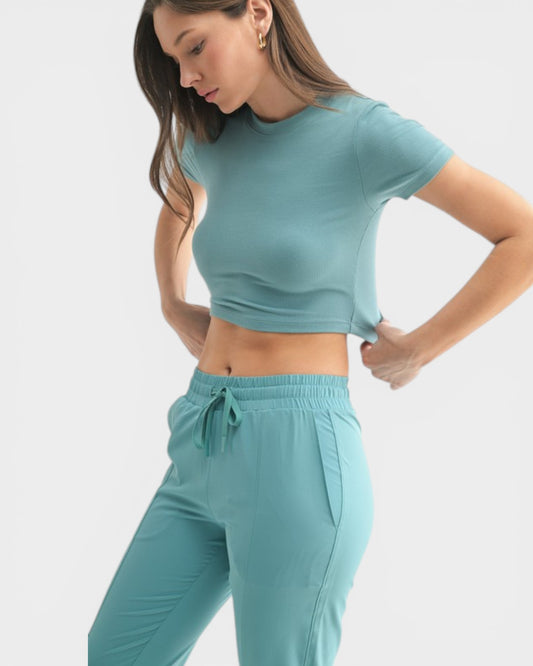 Woman wearing a teal crop top and pants on a white background