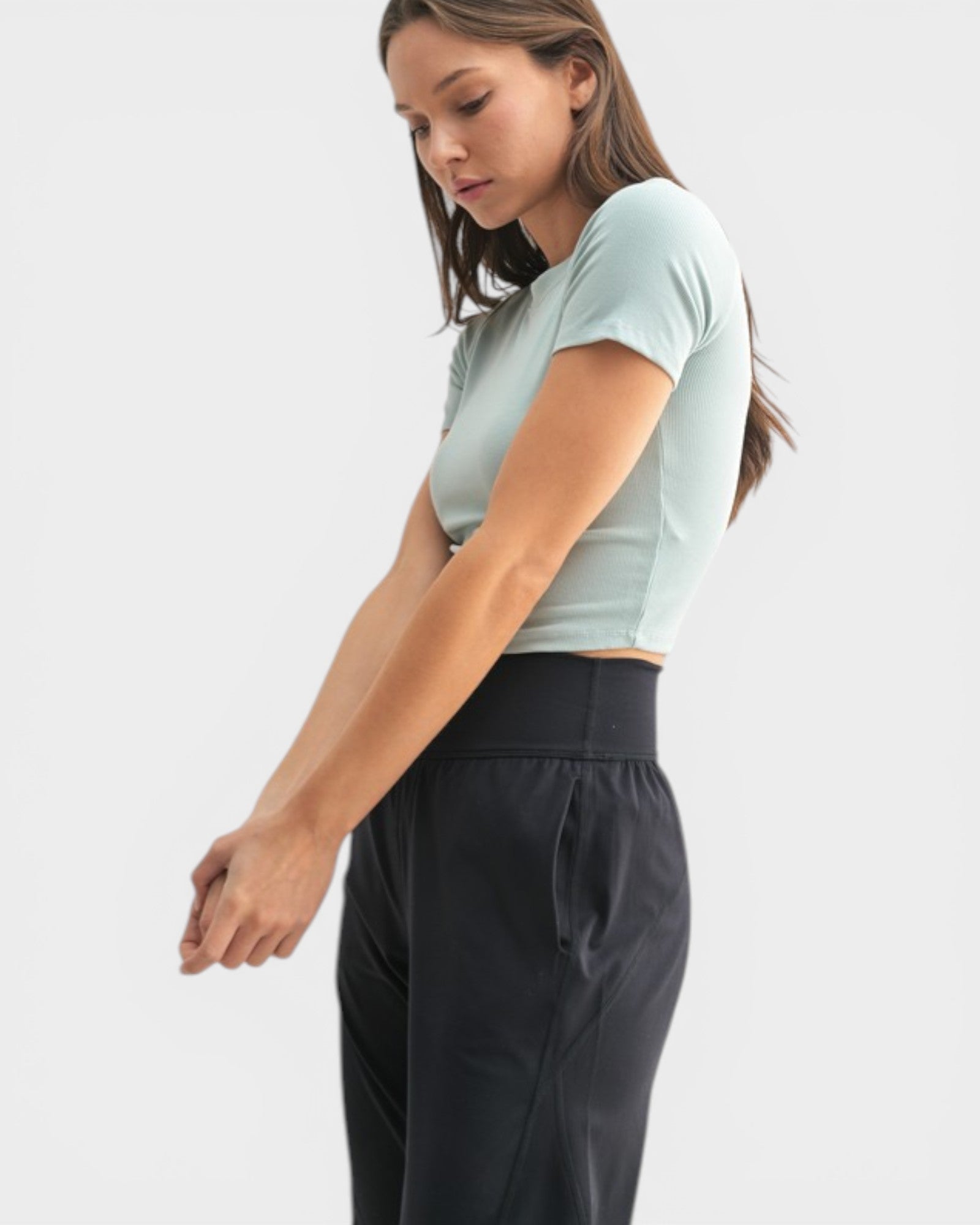 Woman wearing a light green crop top and black pants on a white background