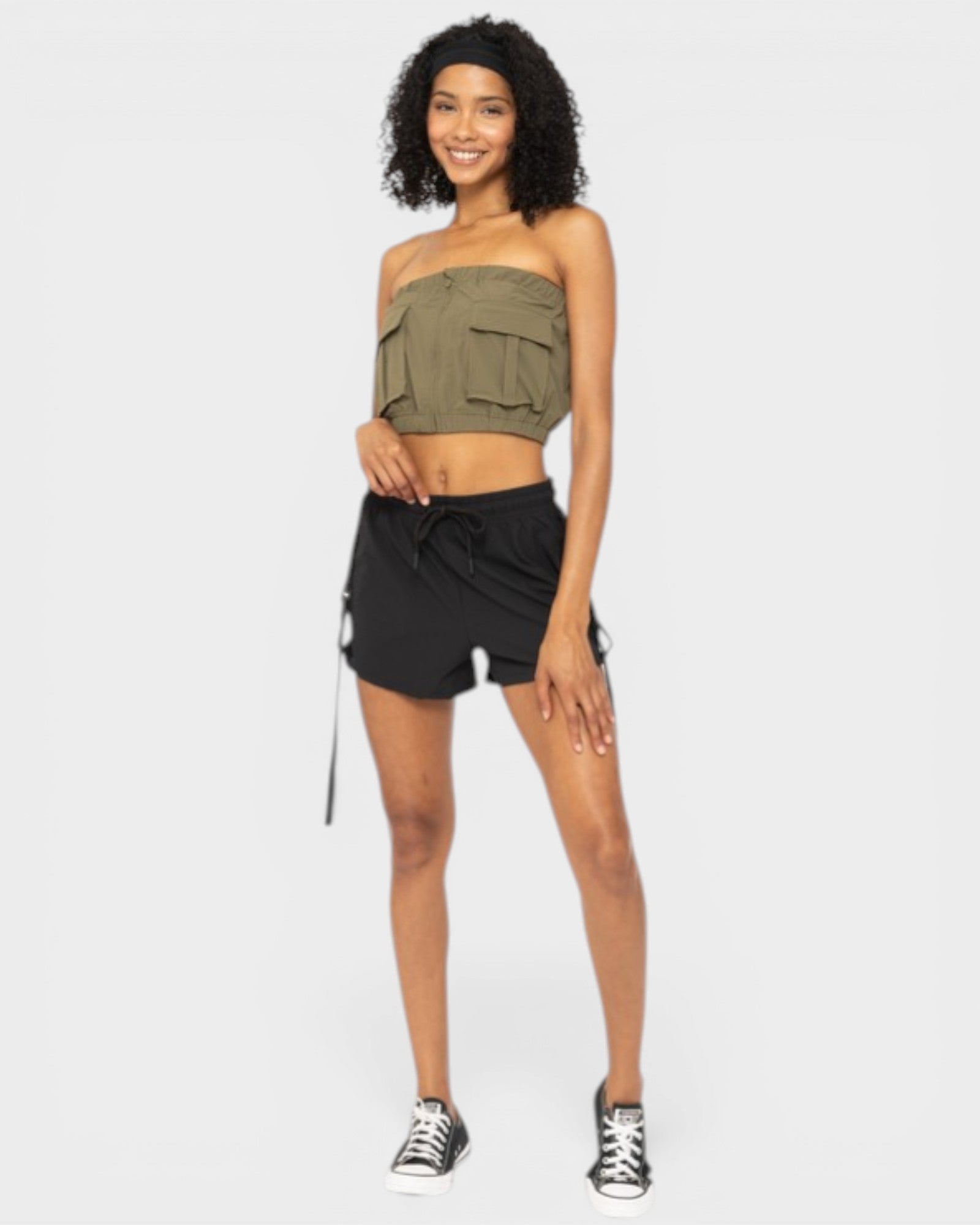 Woman wearing an olive green strapless top and black shorts on a white background
