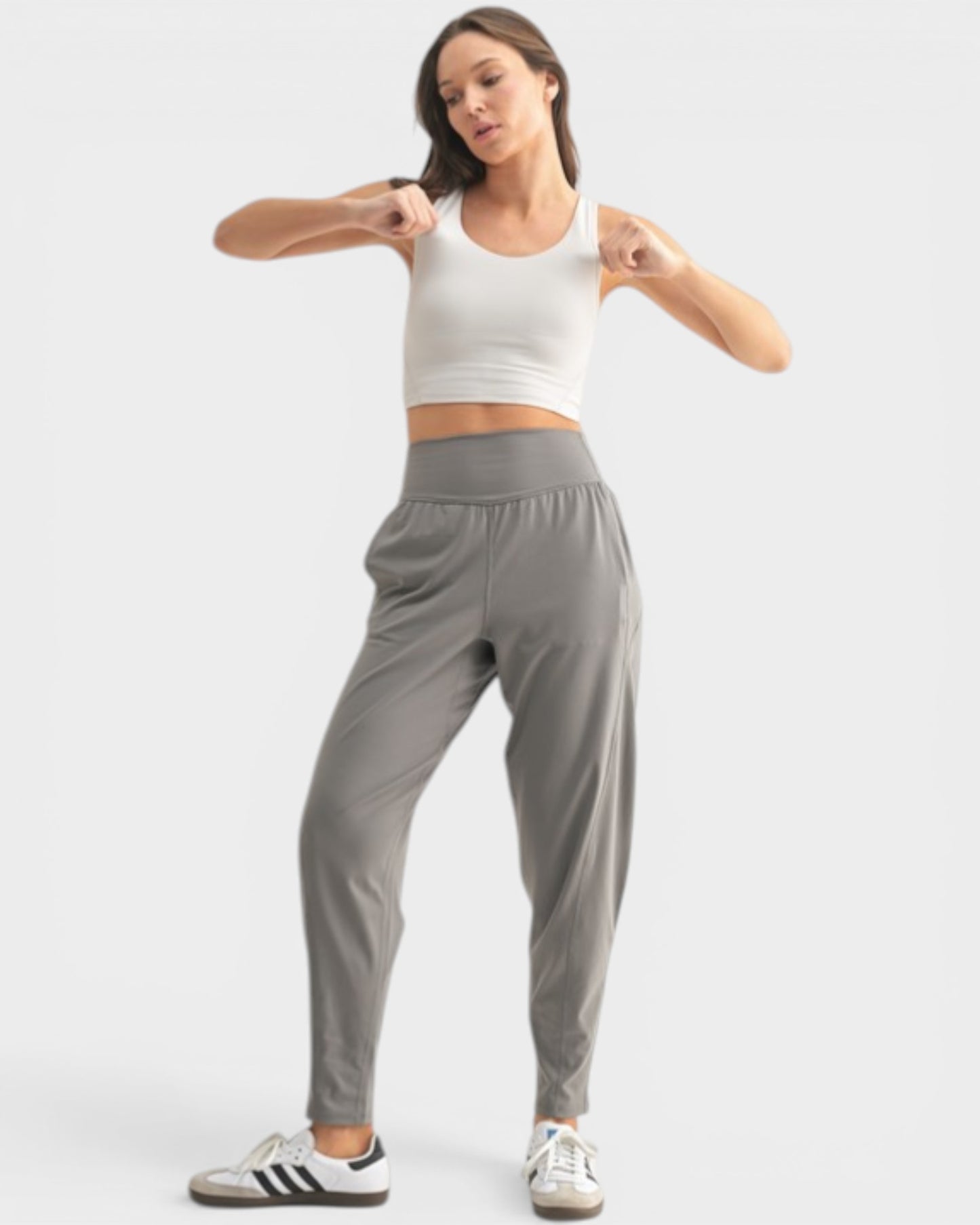 Woman wearing a white crop top and gray sweatpants on a white background