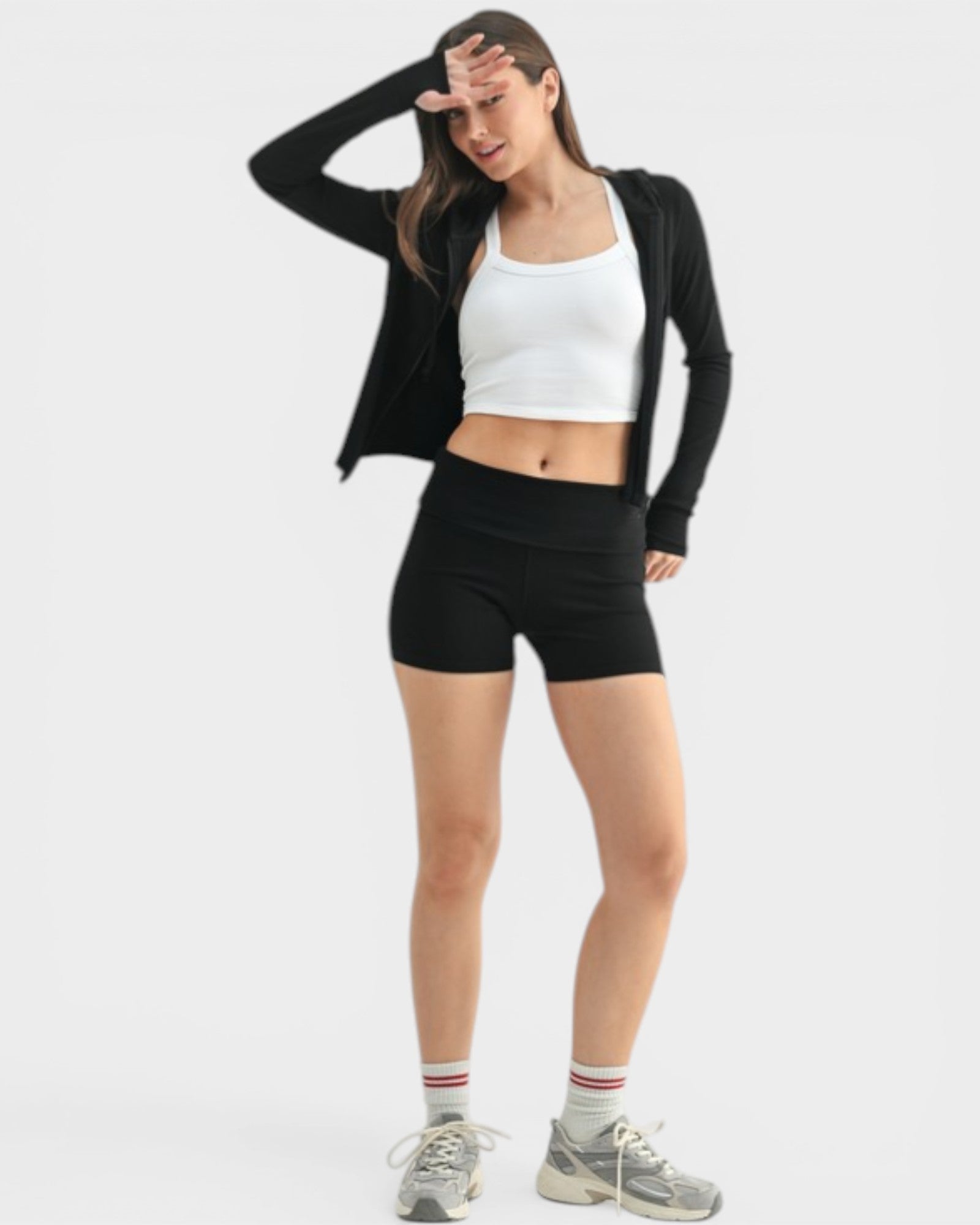 Woman wearing a black cardigan, white crop top, and black shorts on a white background