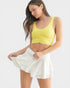 Woman wearing a yellow tank top and white shorts on a light gray background