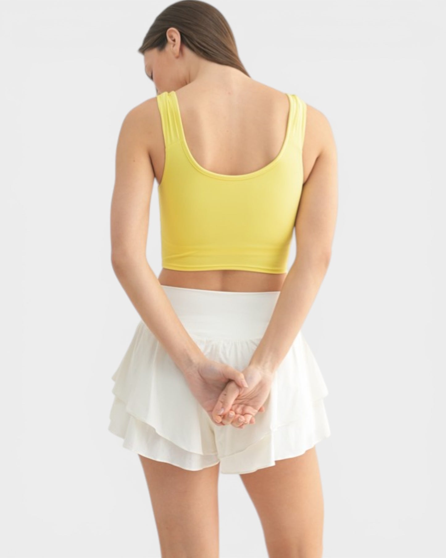 Woman wearing a yellow crop top and white skirt on a light gray background