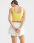 Woman wearing a yellow crop top and white skirt on a light gray background