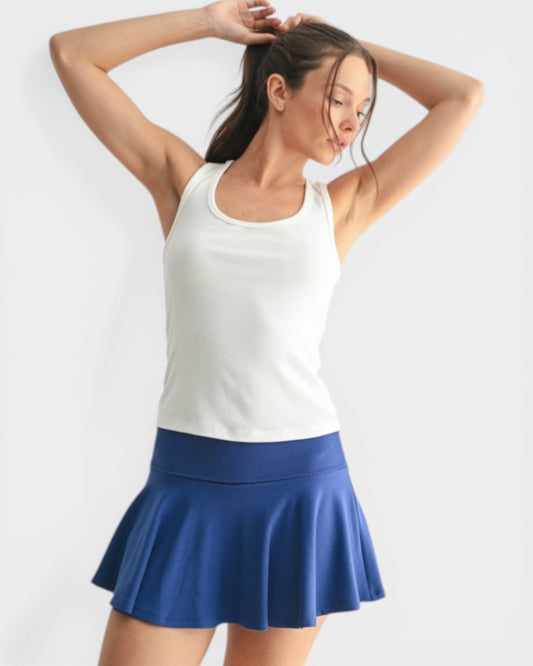 Woman wearing a white tank top and blue skirt on a light gray background
