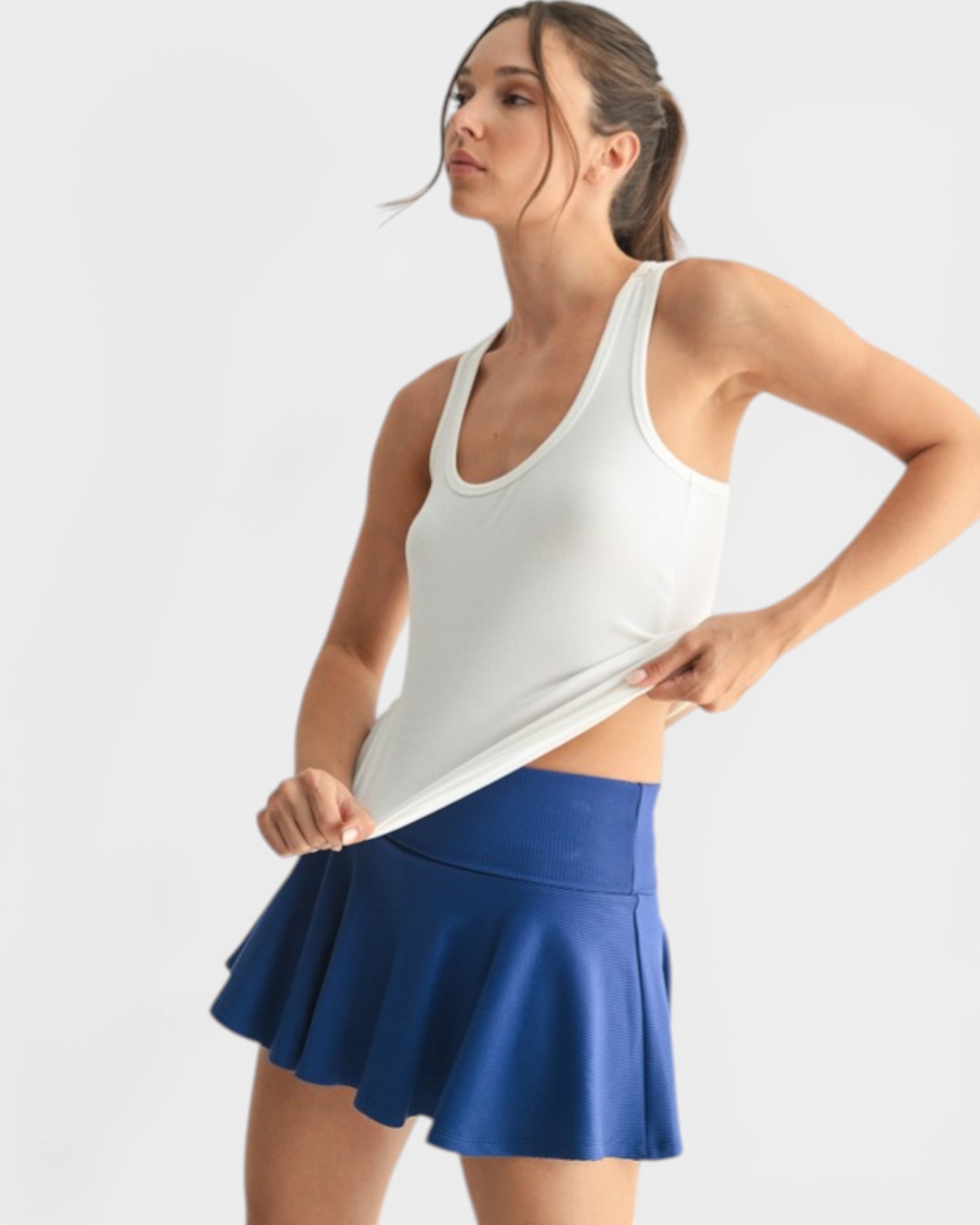 Woman wearing a white tank top and blue skirt on a light gray background