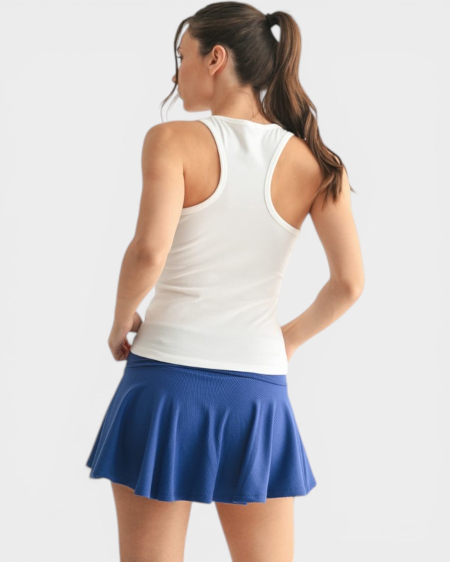 Woman wearing a white tank top and blue skirt on a light gray background