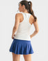 Woman wearing a white tank top and blue skirt on a light gray background
