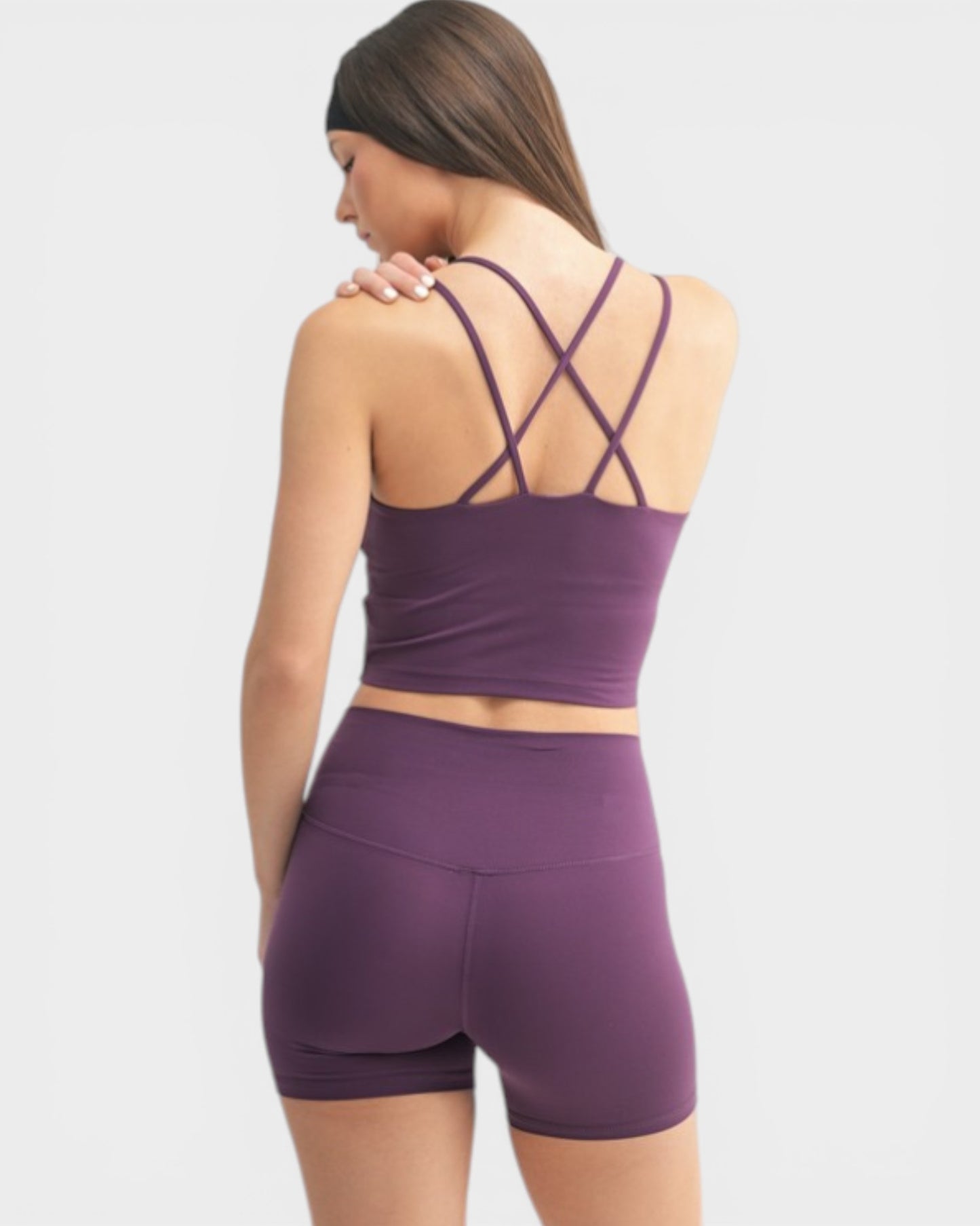 Woman wearing a purple sports bra and shorts set on a light gray background