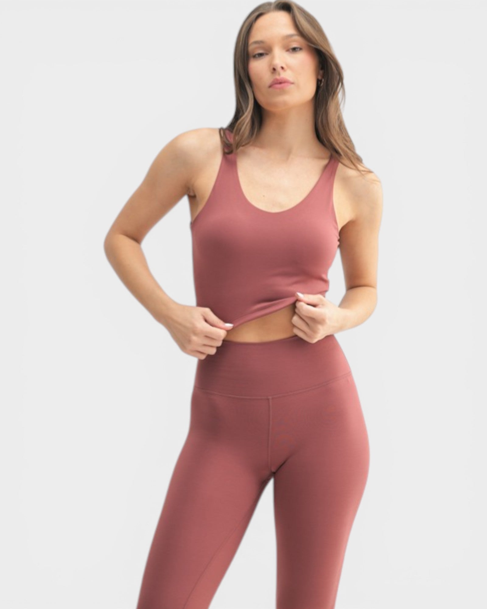 Woman wearing a matching mauve sports bra and leggings set on a light gray background