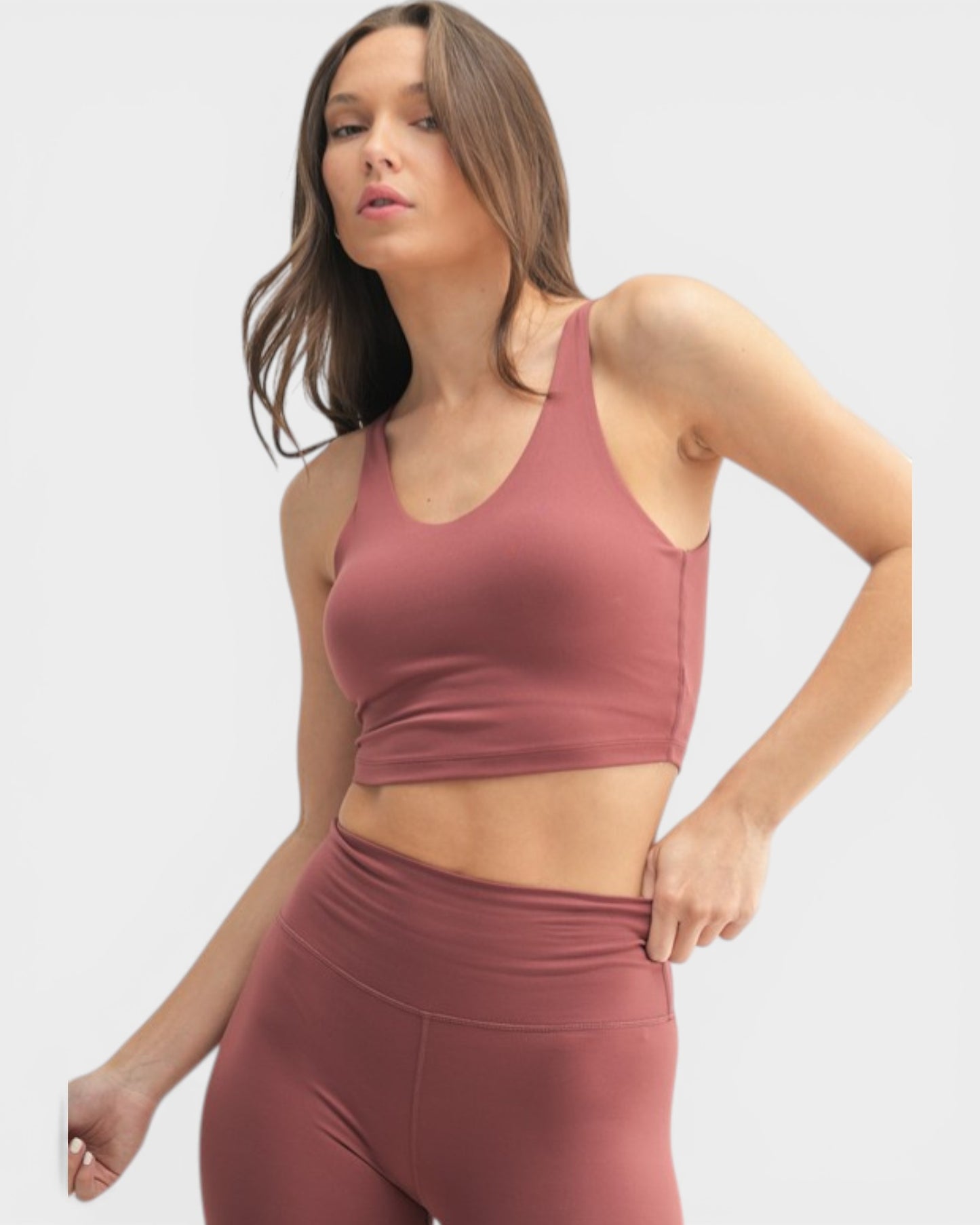 Woman wearing a mauve sports bra and leggings on a white background