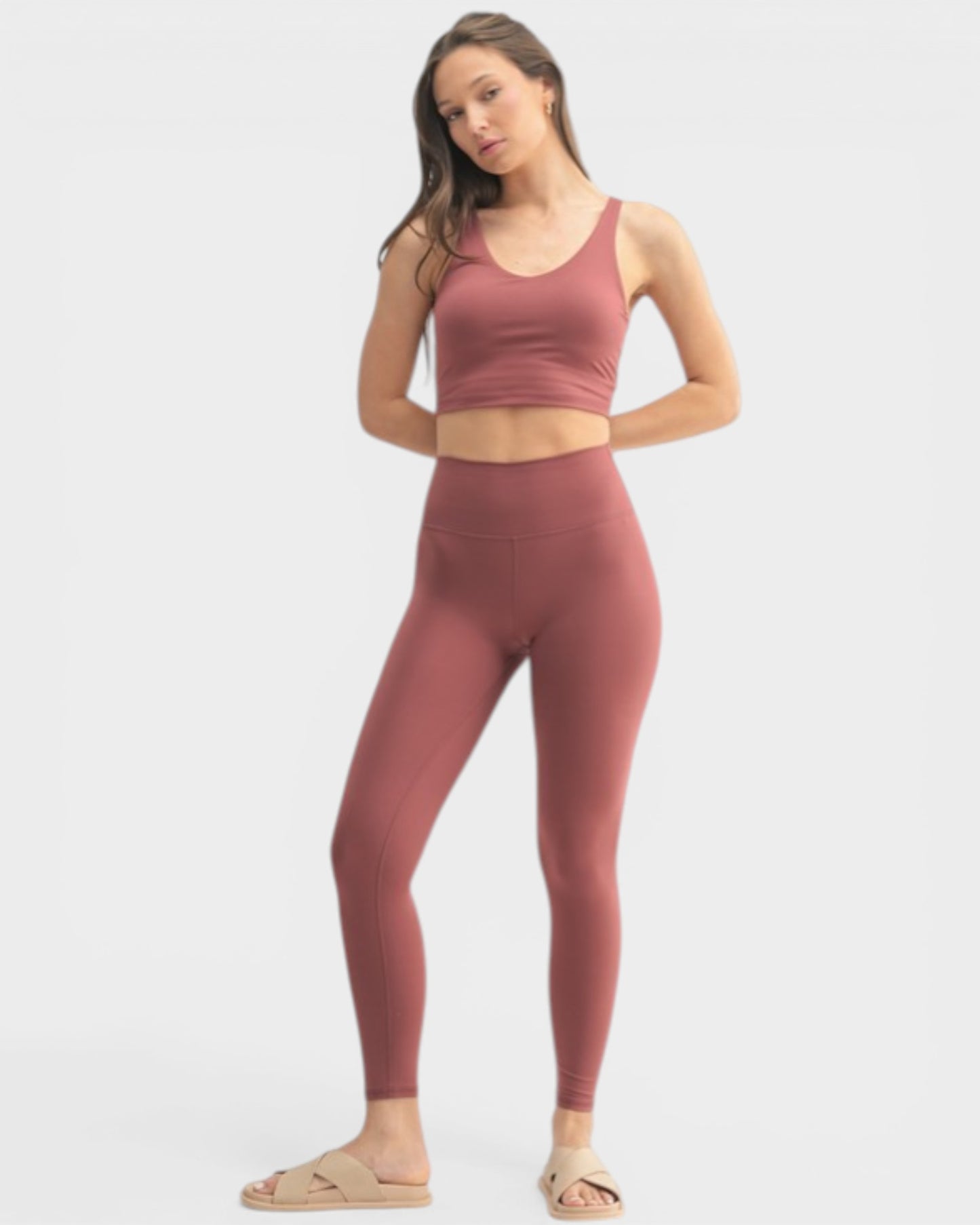 Woman wearing a matching burgundy sports bra and leggings set on a white background