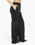 Black wide-leg cargo sweatpants with a side cargo pocket and elastic waistband, shown on a model from the side against a light gray background.