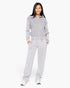 A woman modeling a light gray two-piece loungewear set consisting of a quarter-zip sweatshirt and matching sweatpants, standing against a plain white studio background.