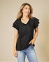 Woman wearing a black top with ruffled sleeves and blue jeans on a beige background