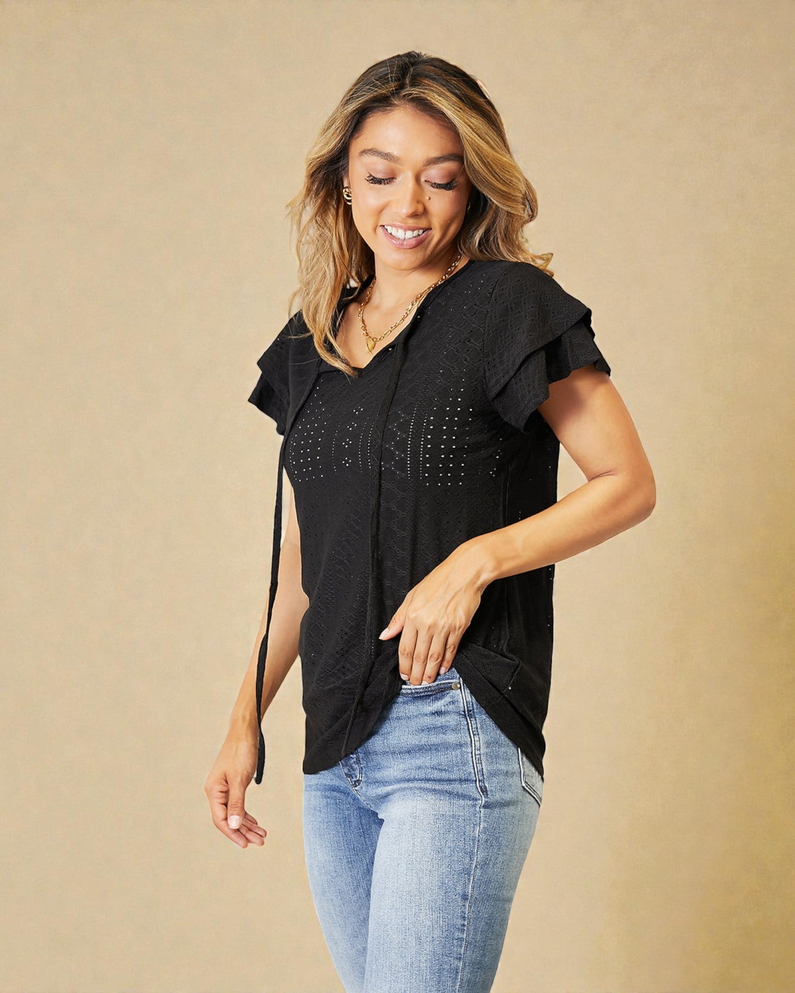 Woman wearing a black top with ruffled sleeves and light blue jeans on a beige background