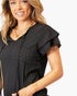 A woman wearing a black short-sleeve eyelet blouse with ruffled sleeves and a V-neckline, shown against a plain white background.