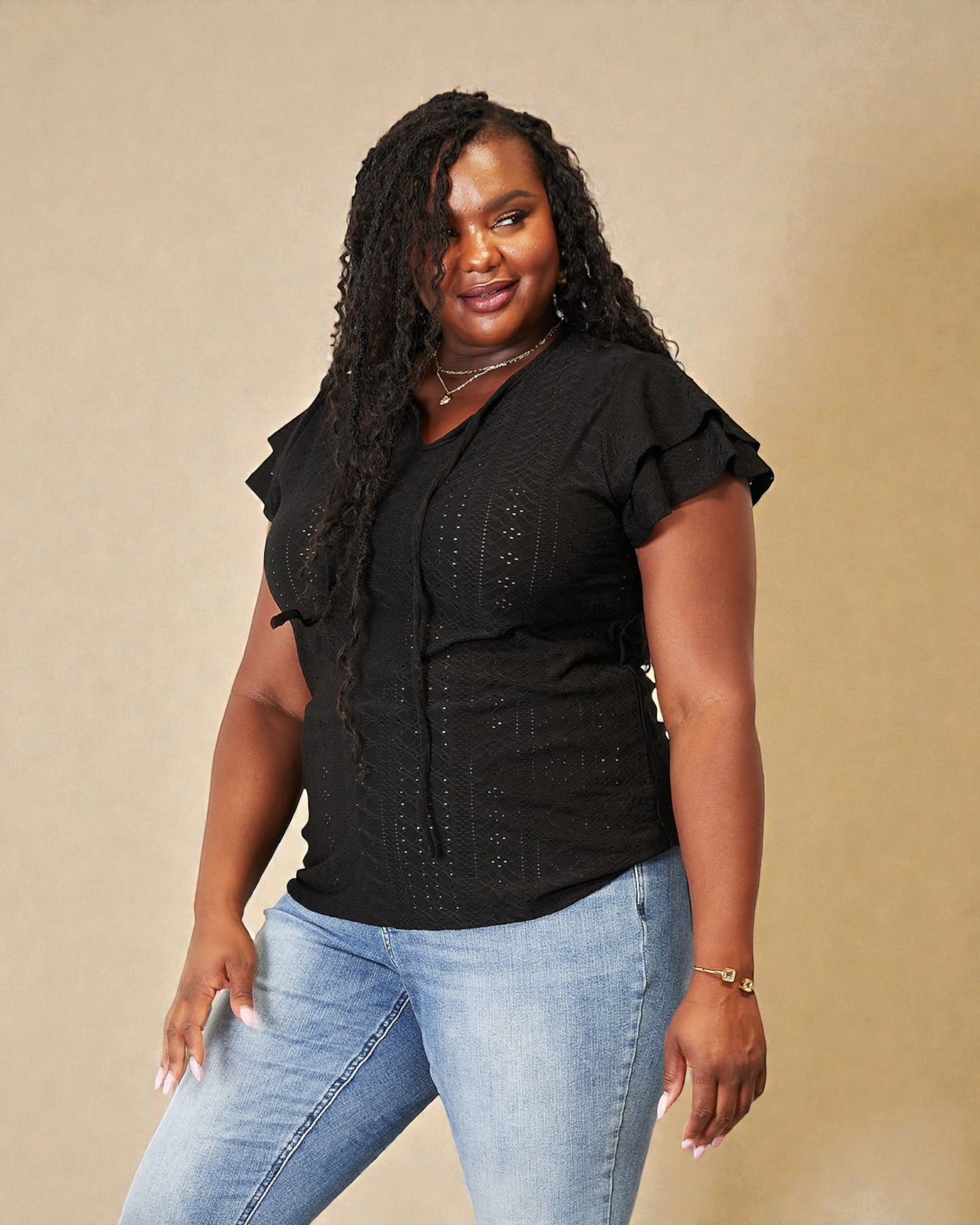 Woman wearing a black top with ruffled sleeves and light blue jeans against a beige background