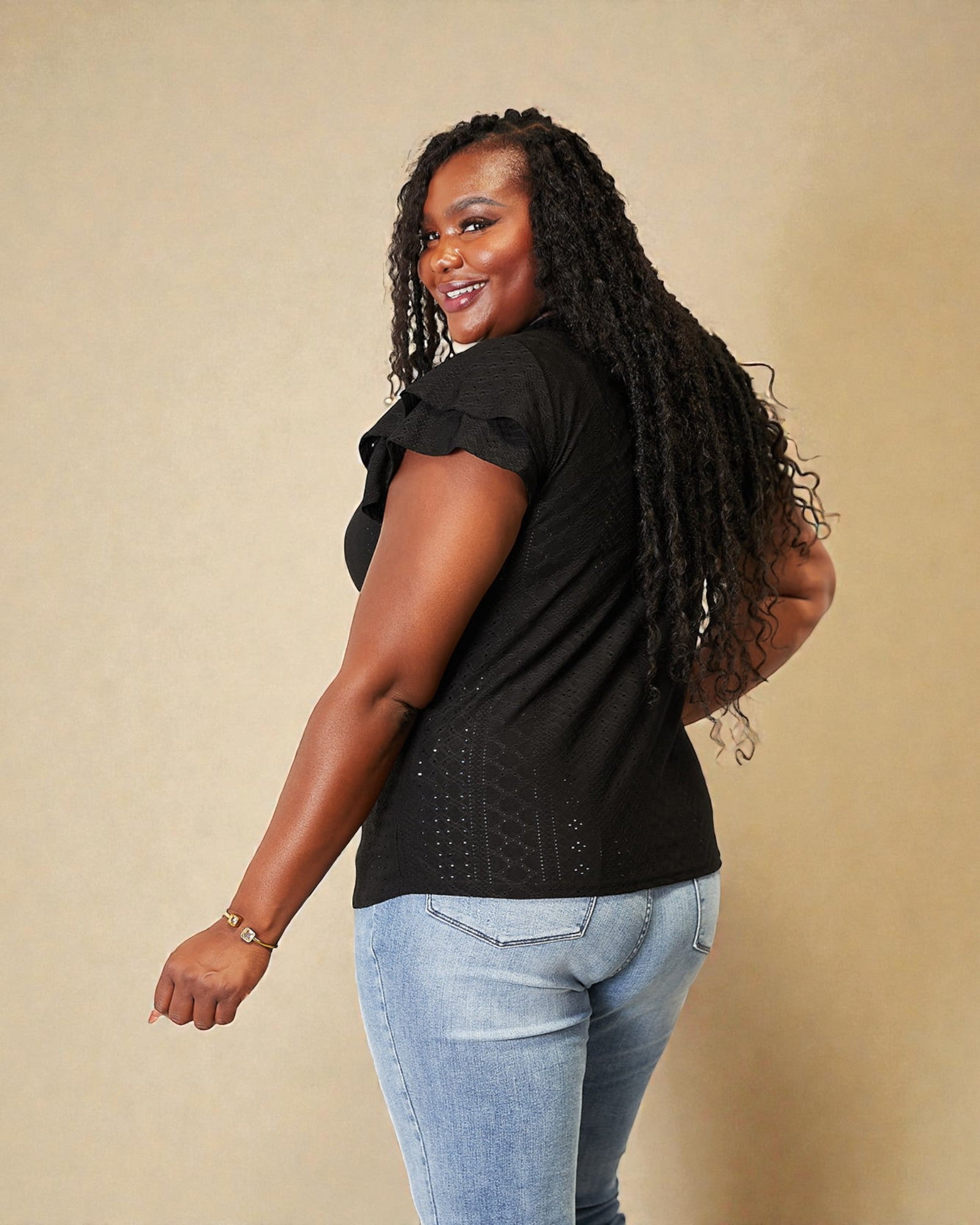 Woman wearing a black top and light blue jeans against a beige background