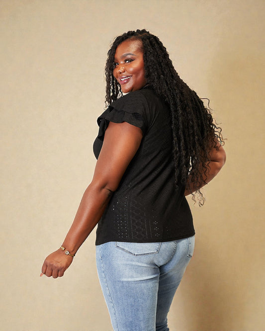 Woman wearing a black top and light blue jeans against a beige background