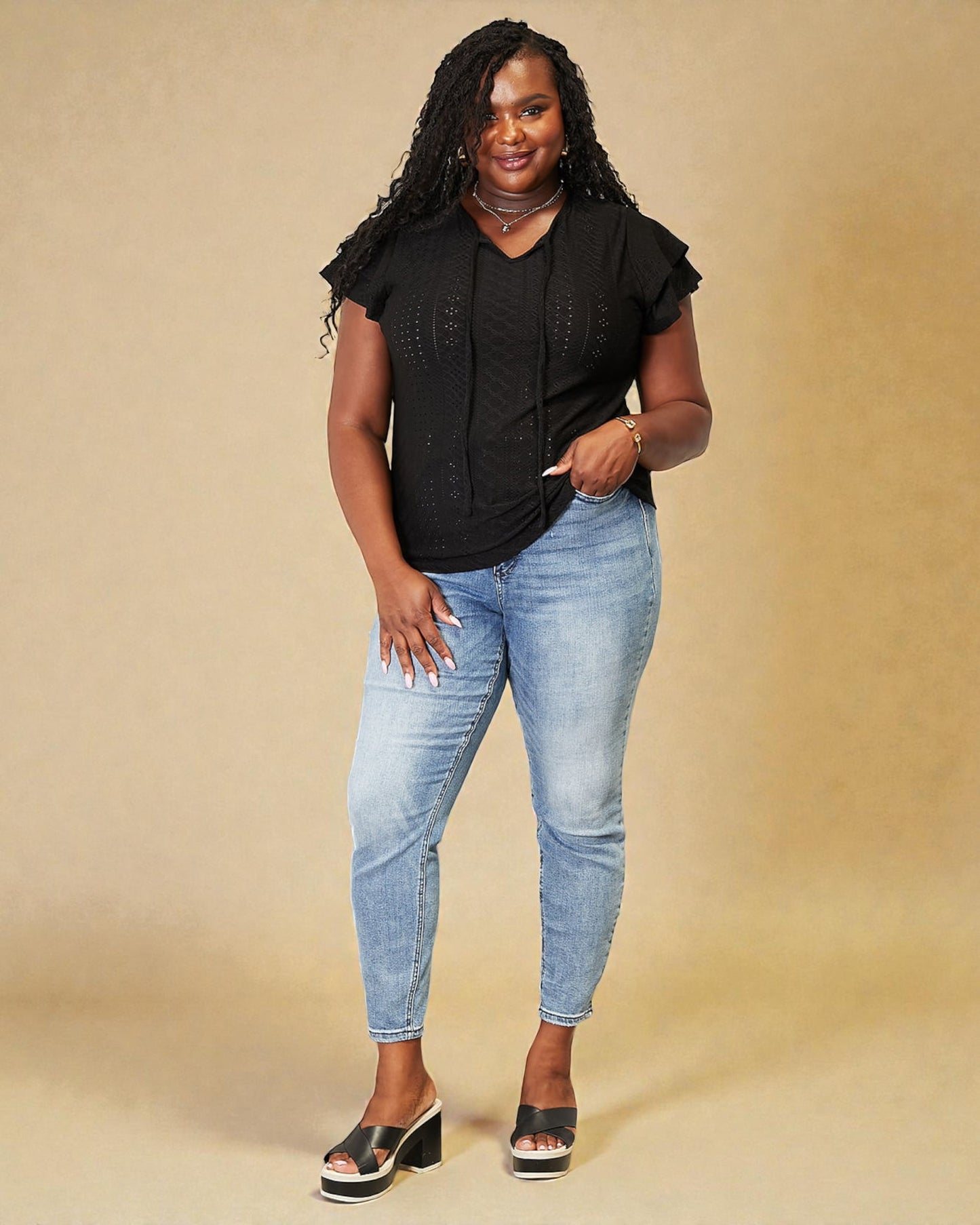 Woman wearing a black top and light blue jeans against a beige background