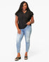 A woman modeling a black short-sleeve top with lace-up front detailing, paired with light-wash blue skinny jeans and black slide sandals, against a plain white studio background.