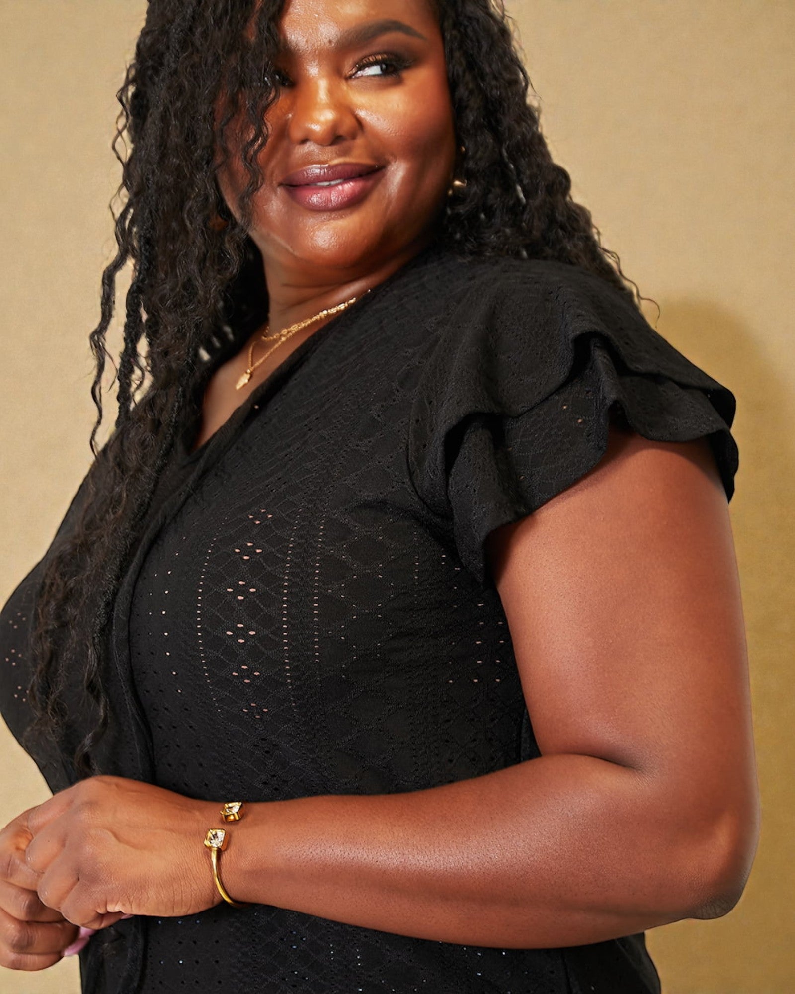 Woman wearing a black dress with ruffled sleeves against a beige background