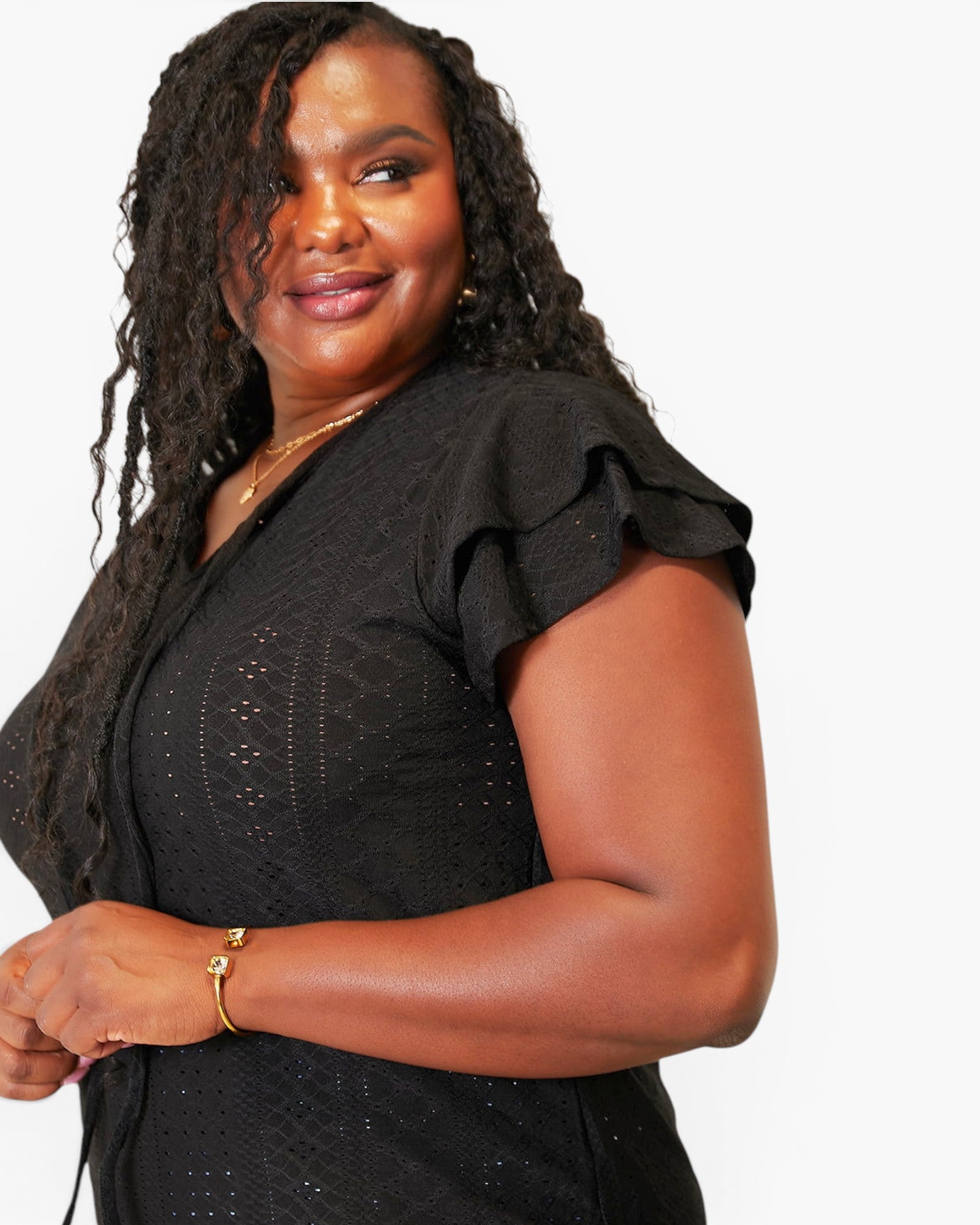 A woman wearing a black short-sleeve V-neck top with ruffled sleeves and subtle textured dot embroidery, photographed against a plain light background.
