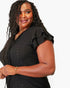 A woman wearing a black short-sleeve V-neck top with ruffled sleeves and subtle textured dot embroidery, photographed against a plain light background.