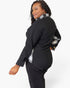 A woman modeling a black long-sleeve top with a silver and black plaid collar and matching plaid shirt underneath, paired with black pants, against a plain white background.