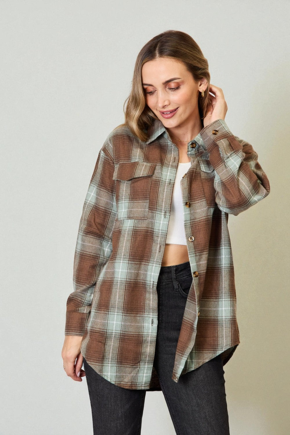 Woman wearing a plaid shirt over a white top and black pants on a plain background