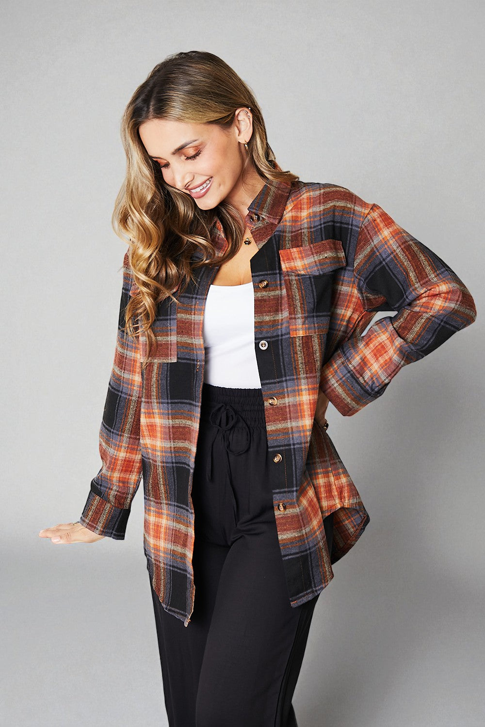 Woman wearing a plaid shirt over a white top and black pants on a gray background