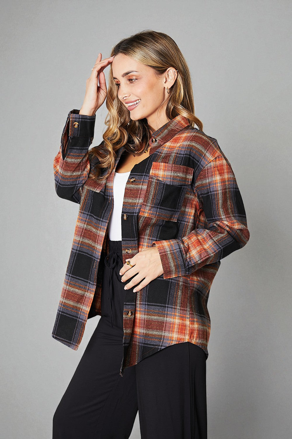 Woman wearing a plaid jacket over a white shirt and black pants on a gray background