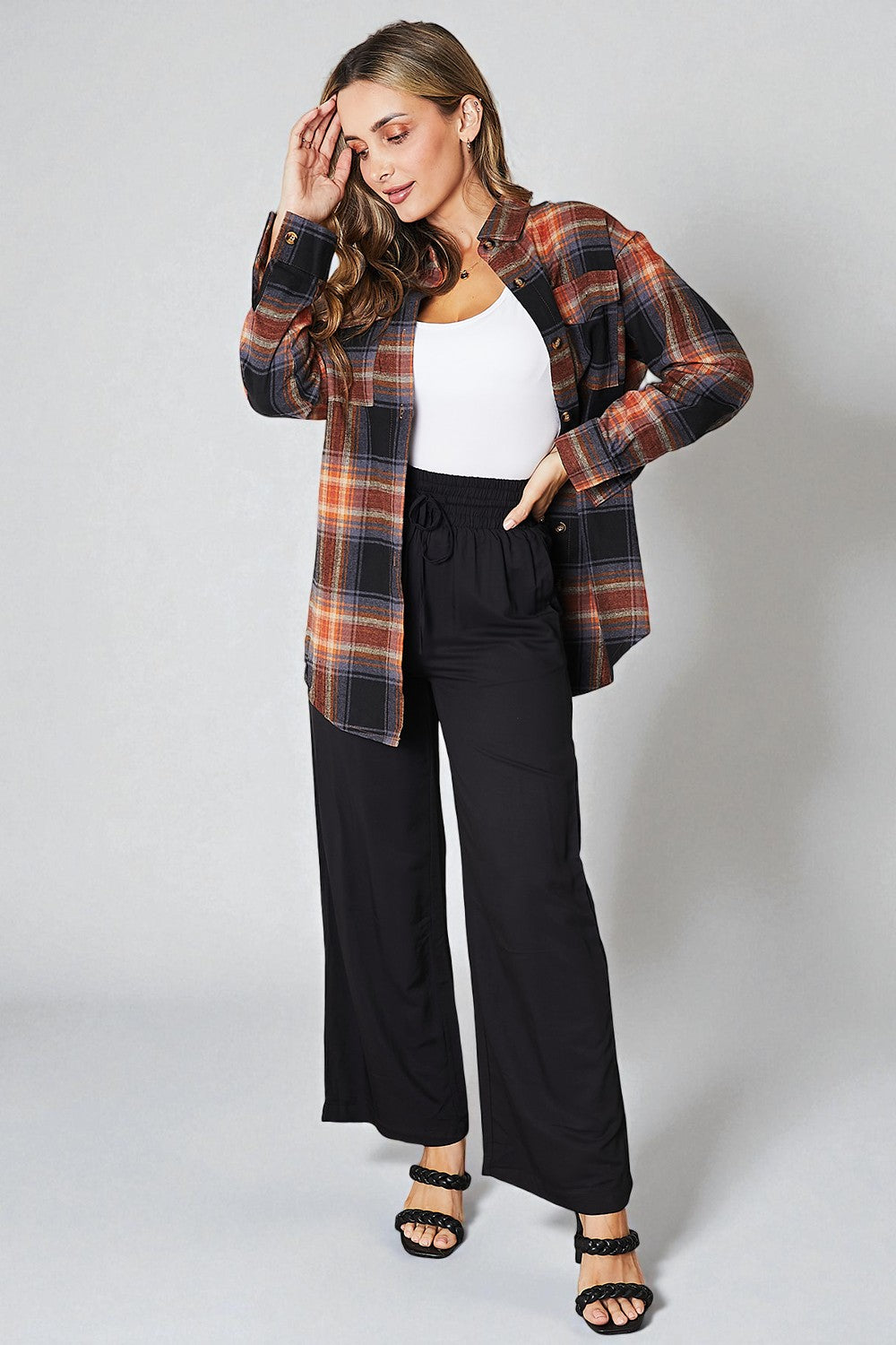 Woman wearing a plaid shirt over a white top and black pants on a plain background