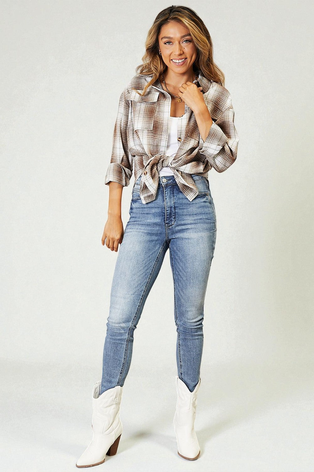 Woman wearing a plaid shirt, white top, blue jeans, and white boots on a plain background