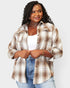 Woman wearing a plaid shirt over a white top and jeans on a light gray background