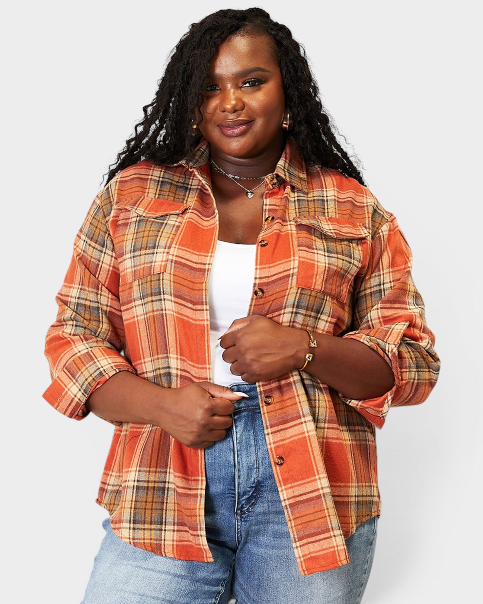 Woman wearing an orange plaid shirt over a white top and blue jeans on a light gray background