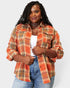 Woman wearing an orange plaid shirt over a white top and blue jeans on a light gray background
