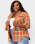 Woman wearing an orange plaid shirt over a white top and blue jeans on a white background