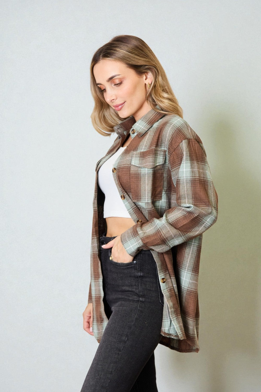 Woman wearing a plaid shirt over a white crop top and black pants on a plain background