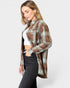 Woman wearing a plaid shirt over a white top and black pants on a light gray background