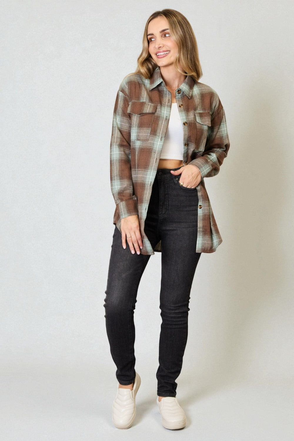 Woman wearing a plaid shirt, white top, and black jeans on a plain background