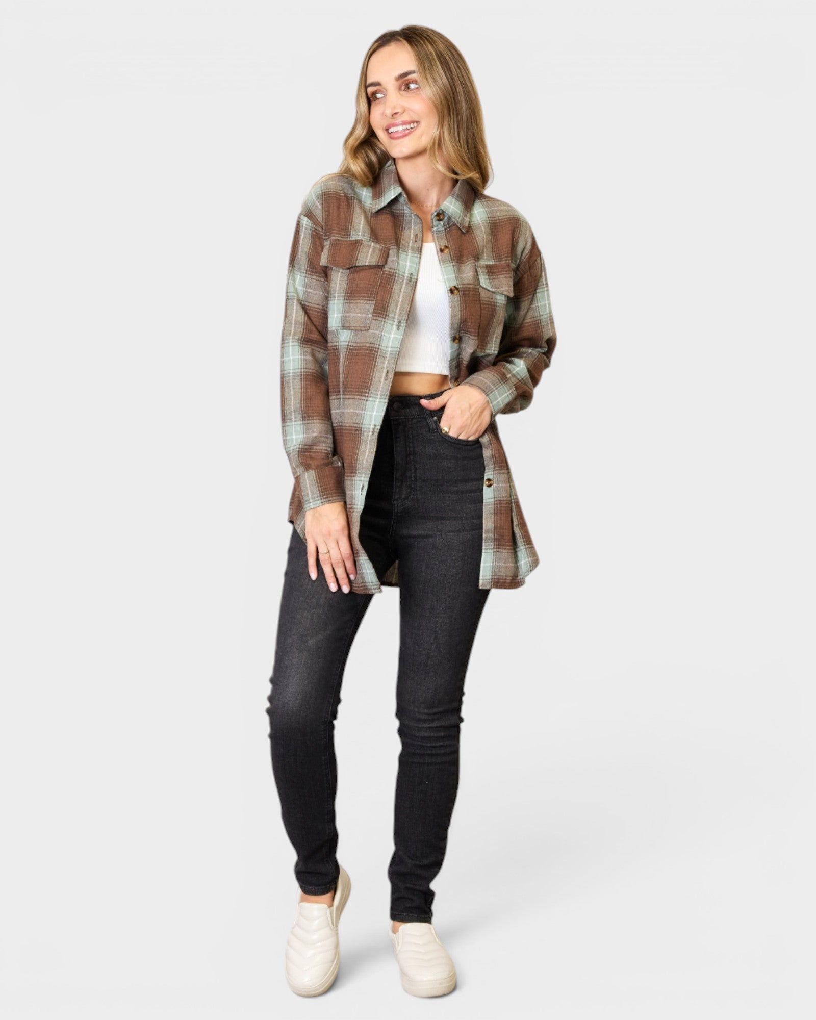 Woman wearing a plaid shirt over a white crop top and black jeans on a white background