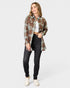 Woman wearing a plaid shirt over a white crop top and black jeans on a white background