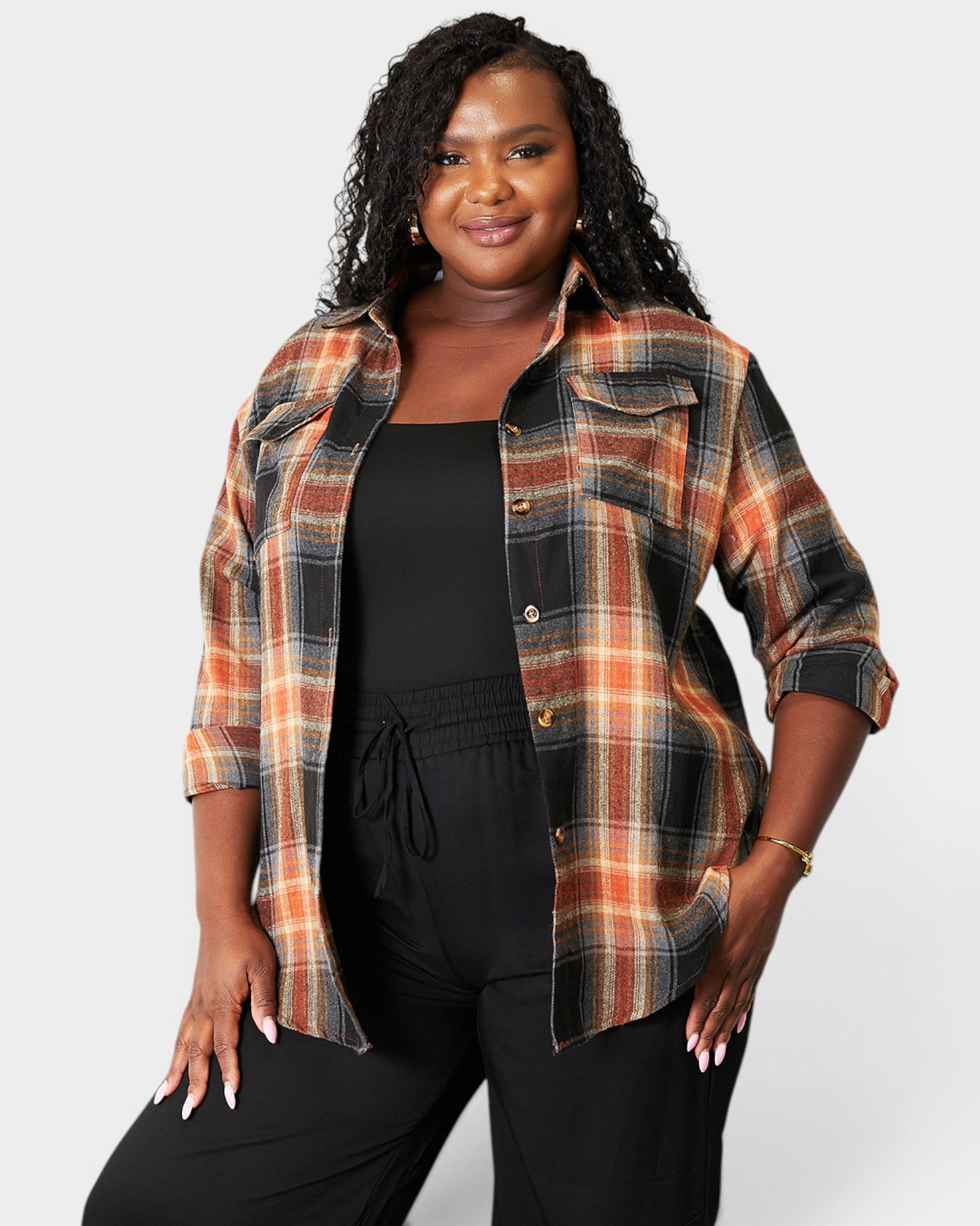 Woman wearing a plaid shirt over a black top and pants on a white background
