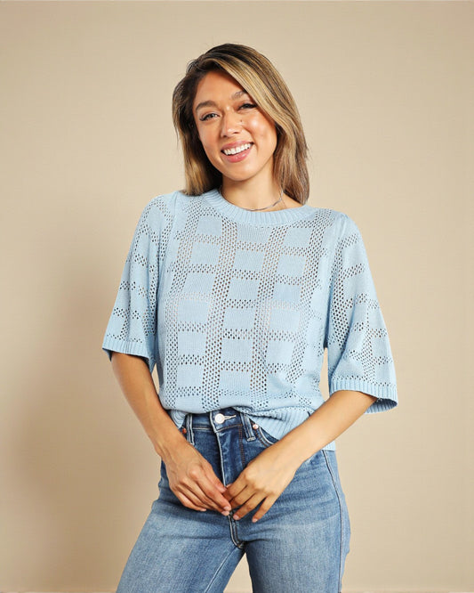 Woman wearing a light blue crochet top and jeans on a beige background