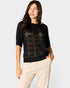 Woman wearing a black patterned sweater and beige pants on a white background