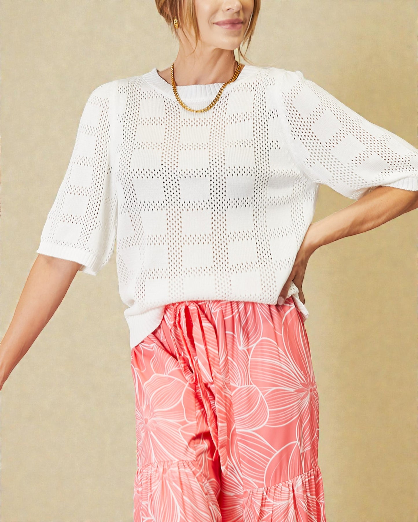 Woman wearing a white perforated top and pink floral pants against a beige background