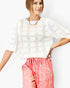 A woman wearing a white short-sleeve knit top with a geometric openwork pattern and pink floral print shorts against a plain white background.