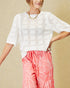 Woman wearing a white perforated top and pink floral pants against a beige background